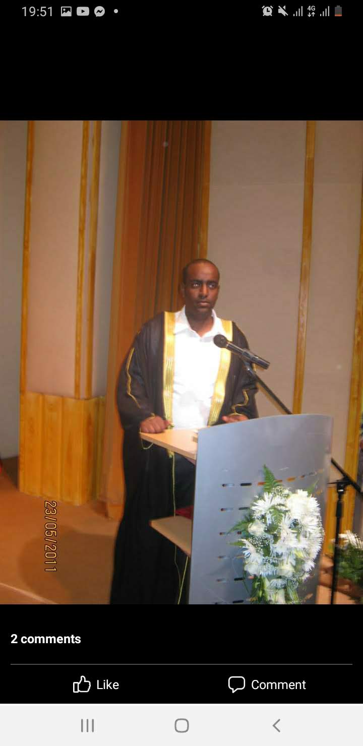 Abdulmuen Mohamed speaking at a podium microphone in ceremonial academic dress during a formal ceremony.