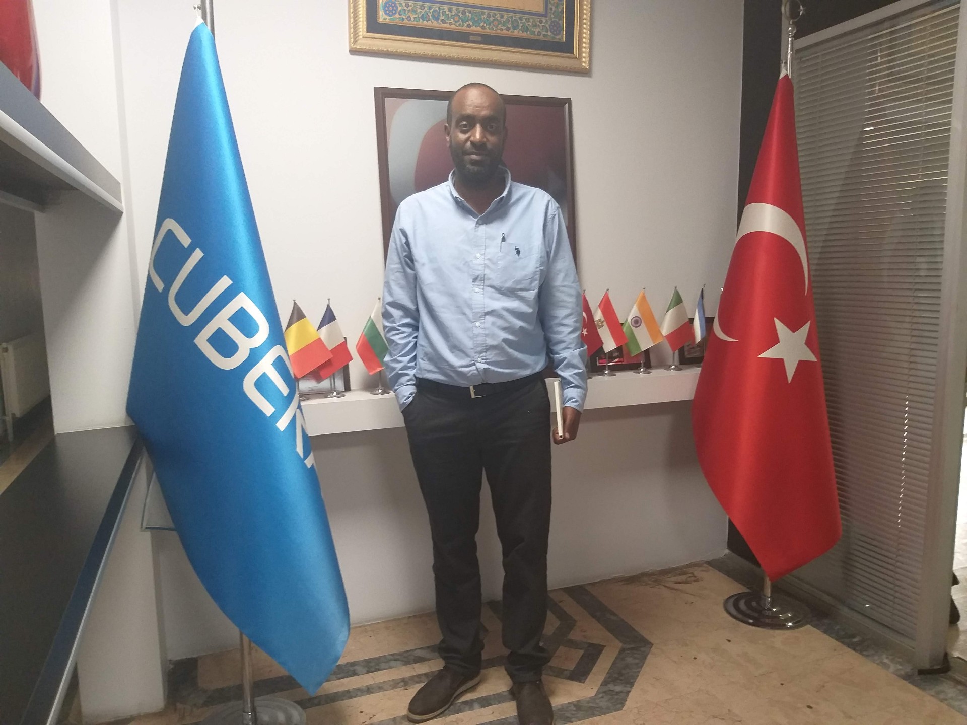 Abdulmuen Mohamed standing in an office reception area beside corporate and national flags.