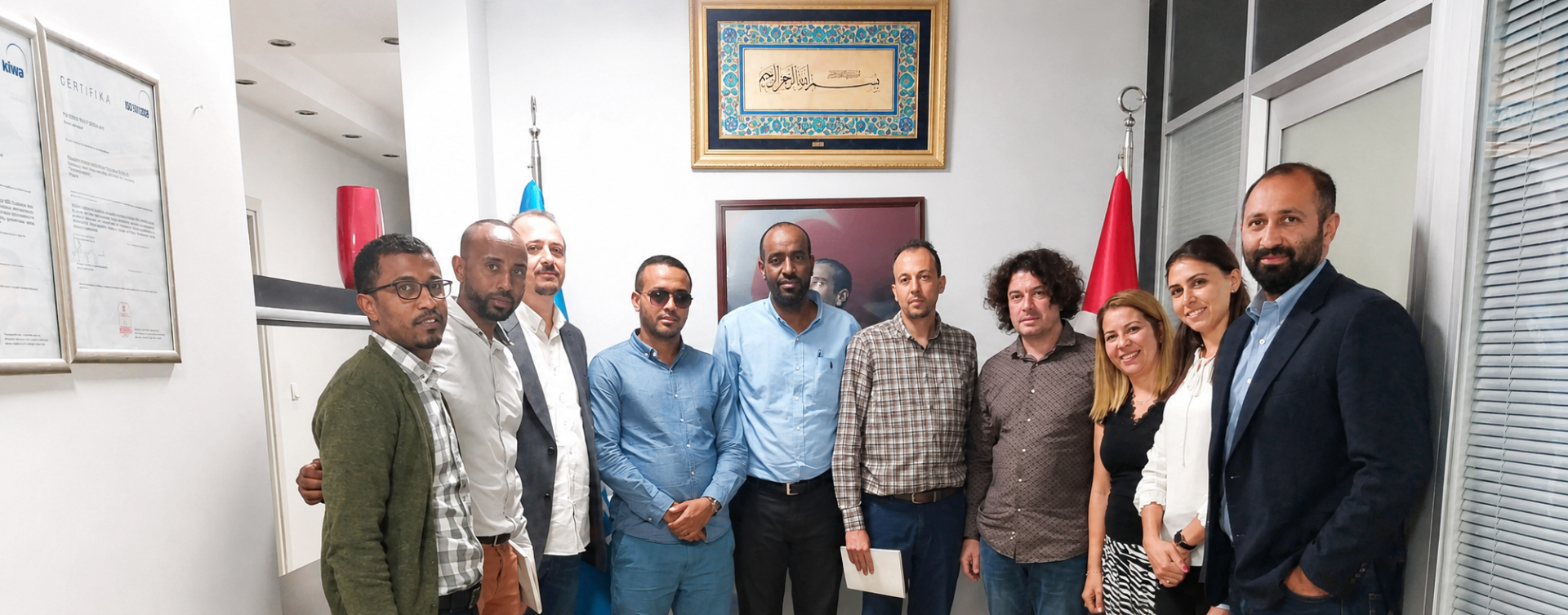 Abdulmuen Mohamed standing with an international business group inside an office, with a Turkish flag beside them.